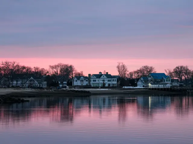 Row of waterfront homes along a still lake under a pink and blue twilight sky, reflected in the water