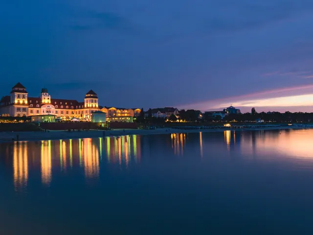 Grand castle-style estate lit up beside the water at twilight with glowing reflections on the surface