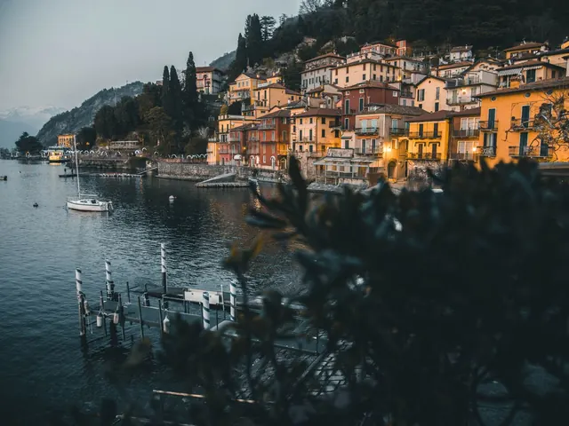 Hillside villas along a lake at dusk with warm lights coming on and boats at private docks