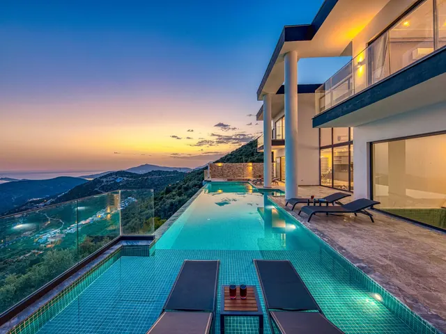Modern oceanview villa with a lit infinity pool and terrace at sunset