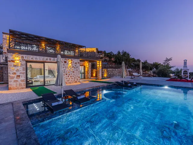 Stone villa with a glowing infinity pool and warm window light at dusk