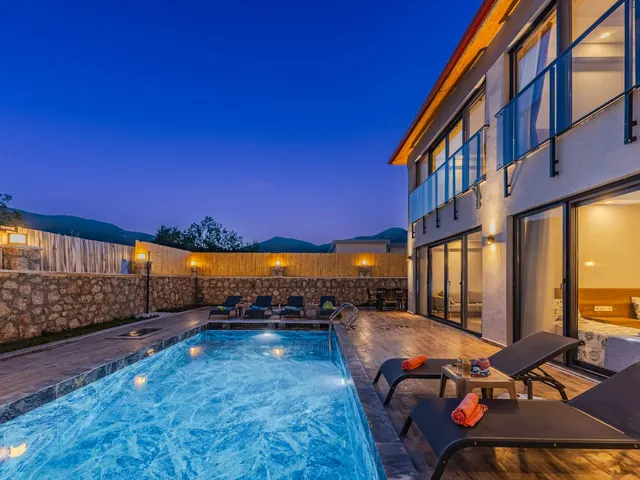 Modern mansion with a lit swimming pool and lounge chairs at twilight