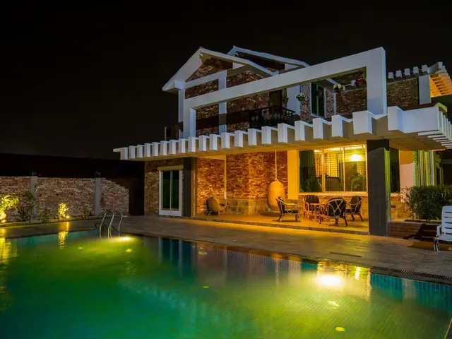 Modern house at night with glowing windows and landscape lighting around an illuminated green pool