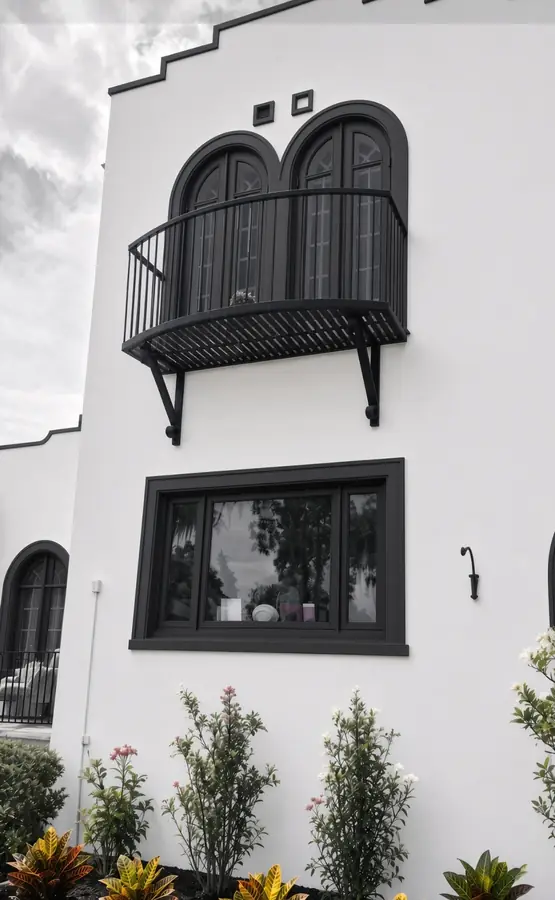 AI concept rendering of a white stucco facade with a stepped parapet, arched windows and a black iron balcony above planted beds