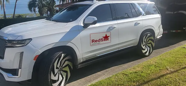 White Cadillac Escalade with a Red Star door sign and black and white wheels parked on a driveway by the water