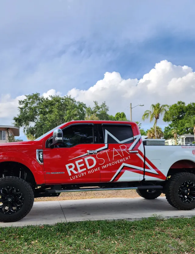 Side view of the lifted red and white Red Star F-250 under a cloudy sky