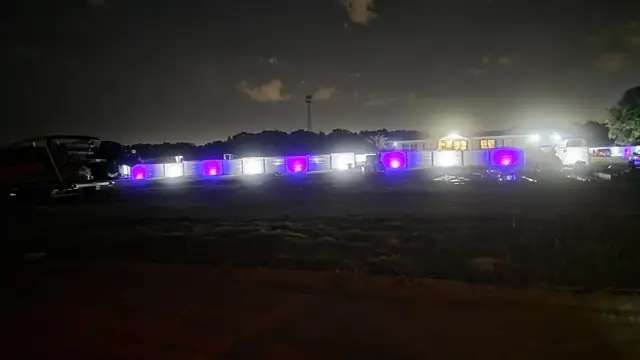 The finished property at night, with a long fence line lit by alternating white and purple lights