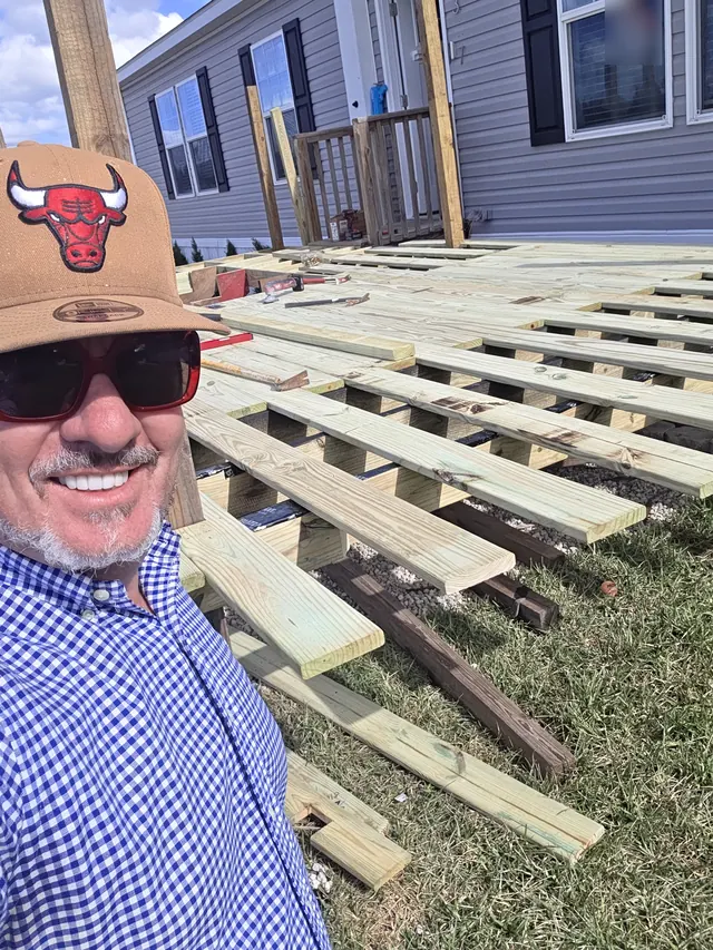 Smiling man in a tan cap, sunglasses and a blue gingham shirt beside a new pressure-treated deck frame