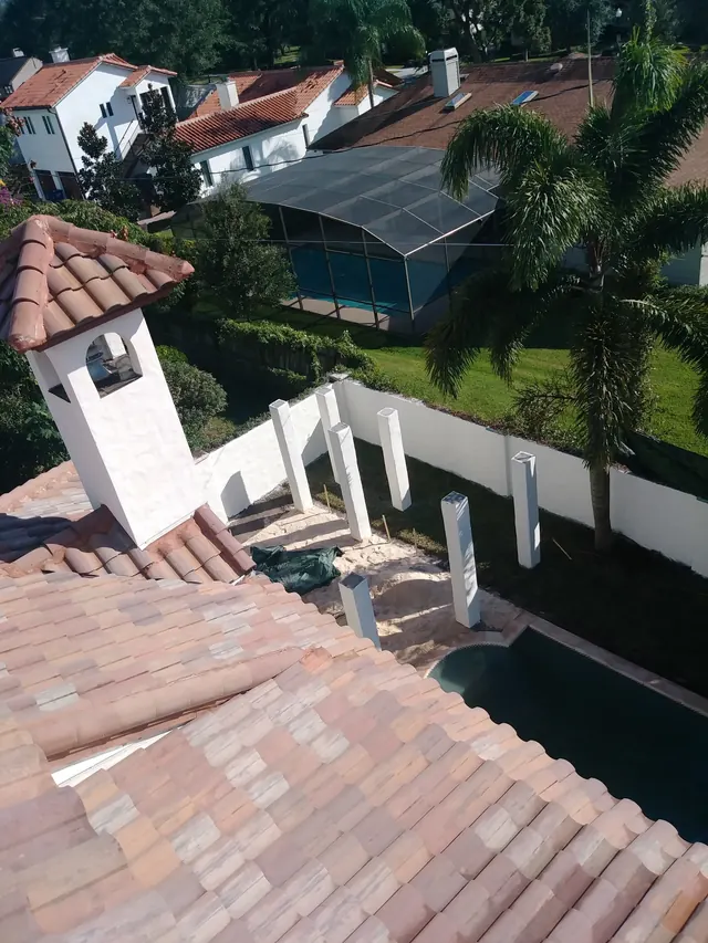 View from a tile roof over a backyard build with white columns going in around a pool and a new white wall