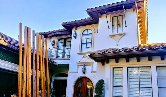 Upright wood slats set beside the arched entry of a white stucco Mediterranean-style home with a tile roof